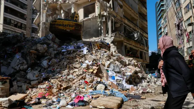 A woman watches as a bulldozer clears the rubble of a destroyed building the day after an Israeli airstrike in the Ain Mreisseh neighborhood of Beirut, Lebanon