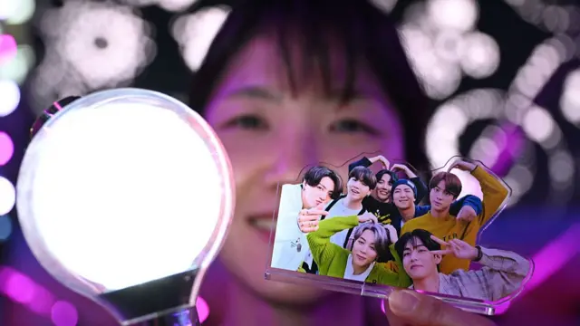 A fan of K-pop boy band BTS holding an 'ARMY Bomb' and a picture of BTS members
