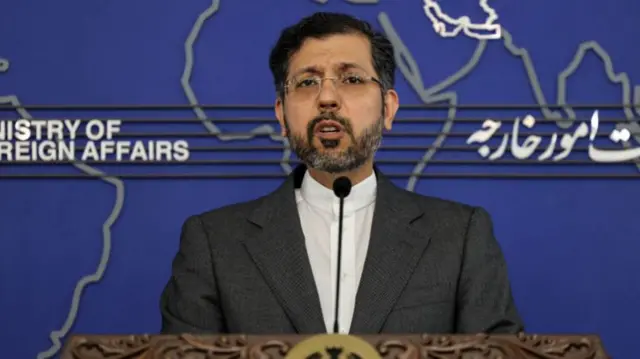 Saeed Khatibzadeh speaks behind an ornate wooden lectern in front of a large map of the world.