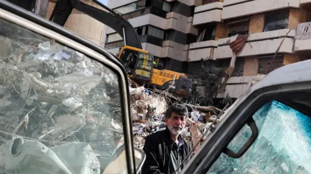 A man stands near a damaged vehicle and rubble at the site of an Israeli strike in Tallet El Khayat in Beirut