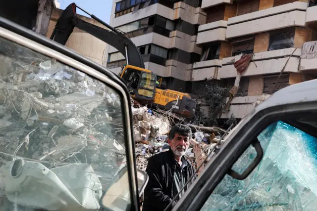 A man stands near a damaged vehicle and rubble at the site of an Israeli strike carried out on Wednesday, in Tallet El Khayat in Beirut, Lebanon