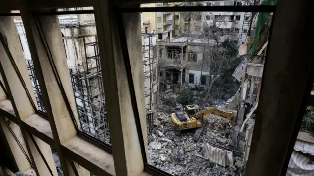 Heavy machinery operates as people gather at the site of an Israeli strike carried out in Beirut - as seen from inside a building