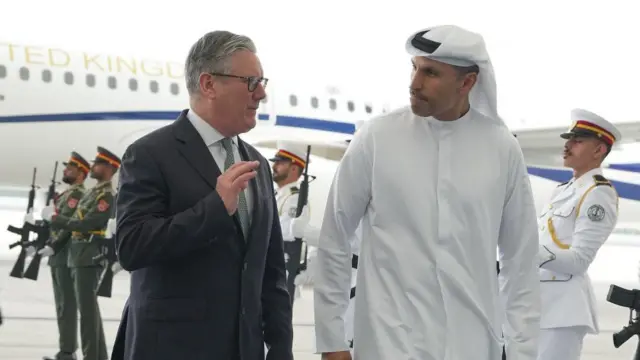 Starmer walking alongside Khaldoon Khalifa Al Mubarak in front of a plane. Soldiers stand behind them holding large guns out in front of them