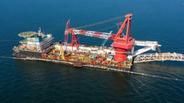 A floating vessel in the sea with people working, a large crane and helicopter pad.