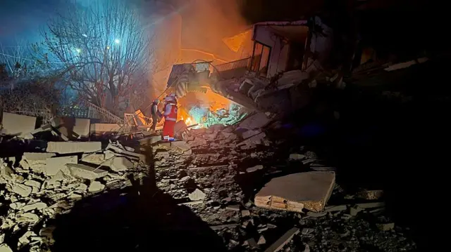 First responders near a building that has been destroyed and turned to rocks and rubble