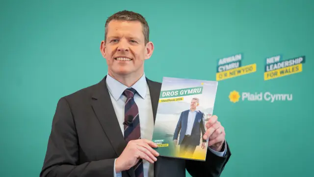 Rhun ap Iorwerth holds up a copy of his party's manifesto