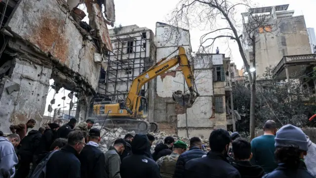Heavy machinery operates as people gather at the site of an Israeli strike carried out in Beirut