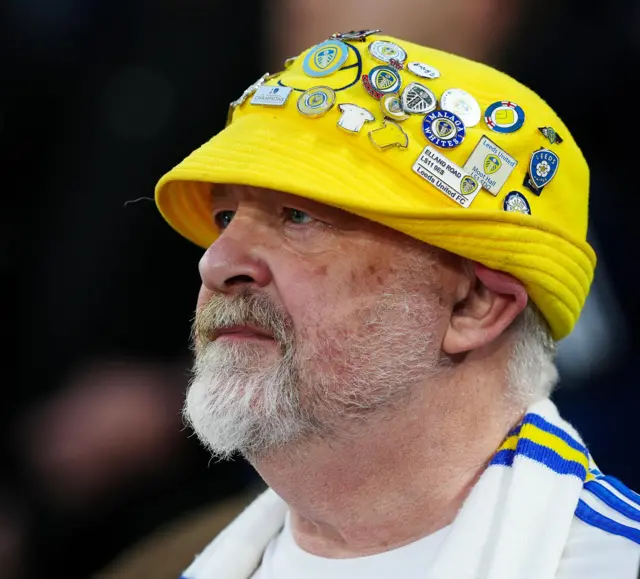 Leeds fan wearing a yellow hat with badges pinned all over it