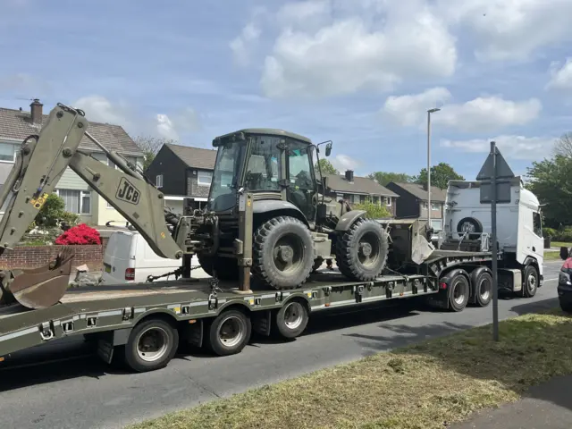 A large digger on the back of a lorry being taken away.