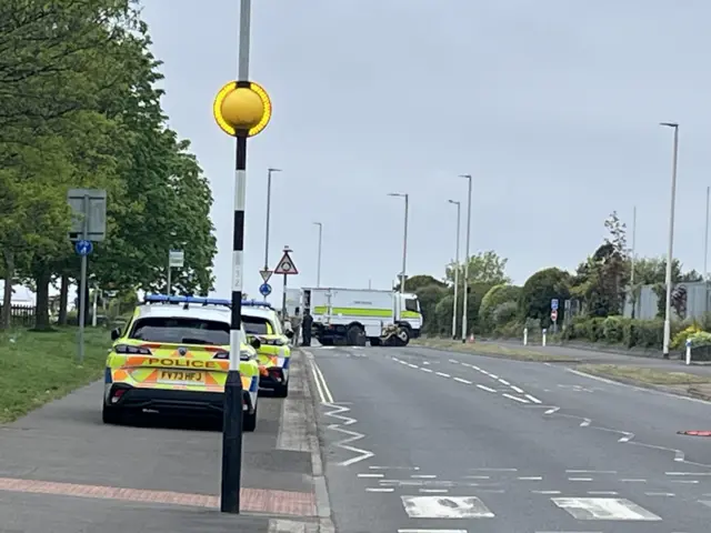Two police cars parked on a pavement with a bomb disposal van in the middle of the road.