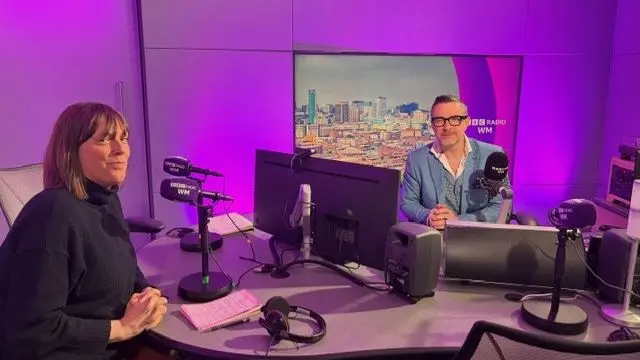 Jess Phillips, in a black jumper, and a man in a blue suit, pose for a photo in the BBC Radio WM radio studio.