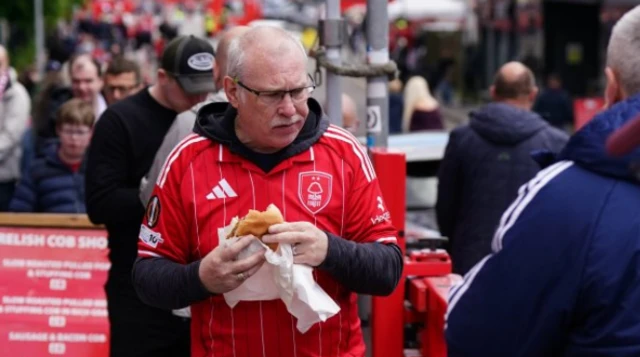 A man wearing a Nottingham Forest shirt and eating a sandwich