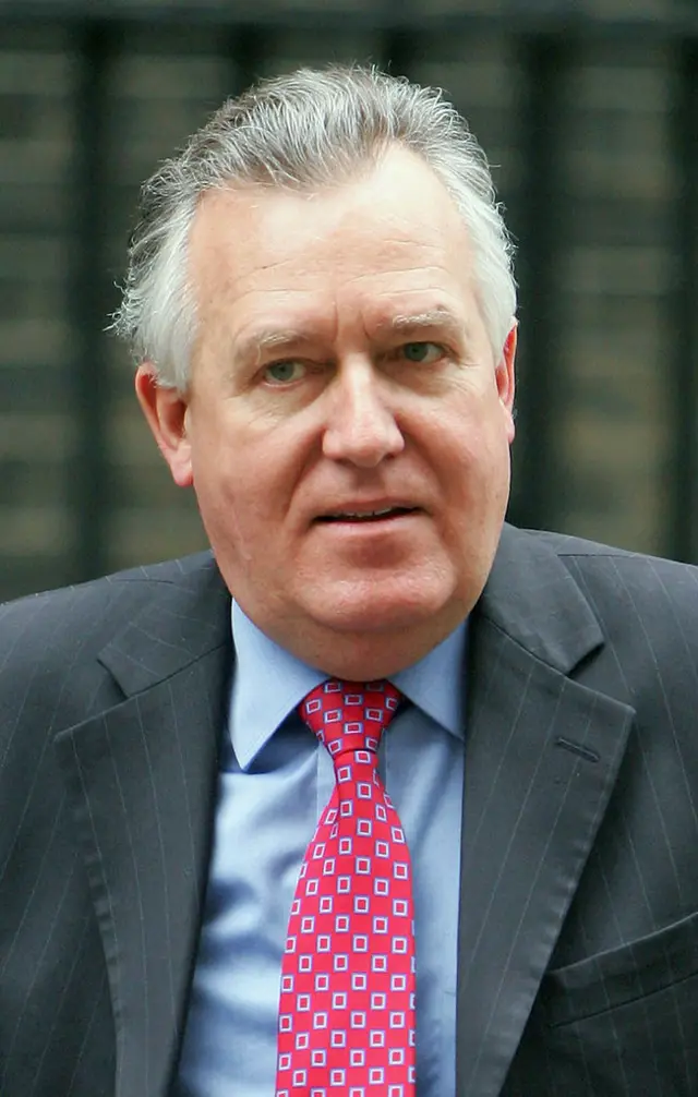 A man in a grey pinstripe suit, a blue shirt and a red tie. He has grey hair.