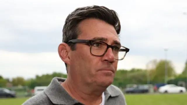 Andy Burnham wears a grey jumper and glasses as he arrives for a charity football match