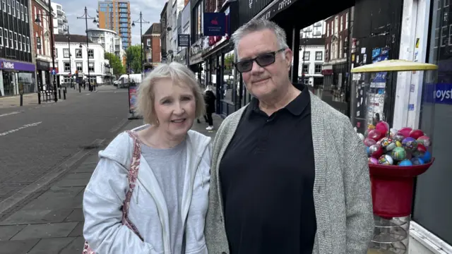 A middle aged couple posing for a photo in an town centre street.