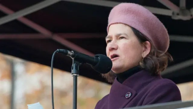 MP Catherine West speaks into microphone wearing purple coat and pink beret