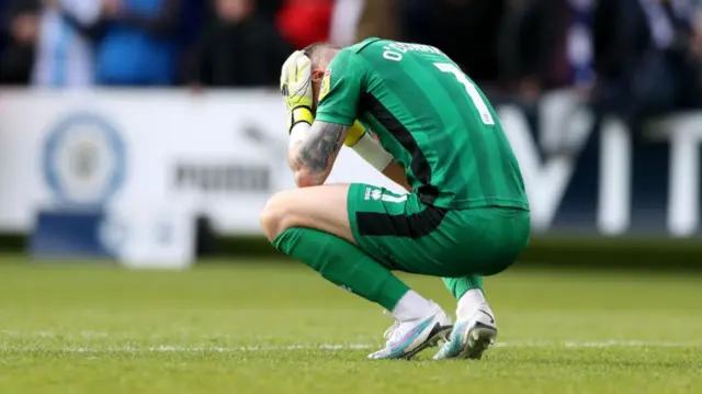 Rochdale goalkeeper Richard O'Donnell crouched with his head in his hands after being relegated in 2023 relegated