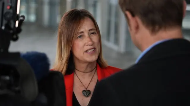 Jane Dodds is speaking to a journalist who is stood next to a camera.