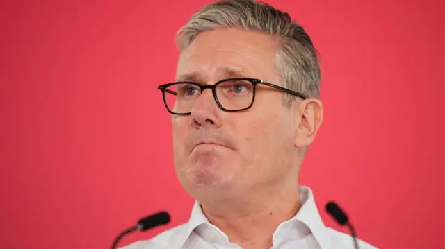Keir Starmer standing in front of a red background and two microphones