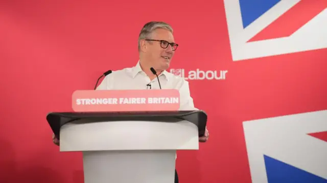 Keir Starmer delivering a speech in London. He is stood at a lectern with a Union Jack