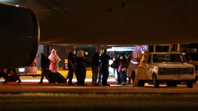 People stand on the tarmac underneath a plane at an airport