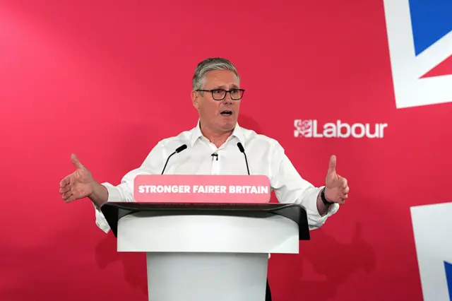 Keir Starmer stood behind a podium that says Stonger, fairer Britain with a union jack and Labour branding behind him.