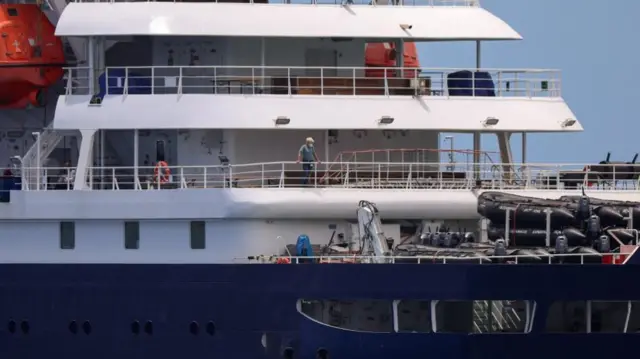 A person with protective gear stands on the deck of the cruise ship MV Hondius