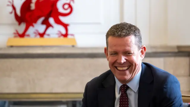Rhun ap Iorwerth sat with a Red Dragon statue behind him