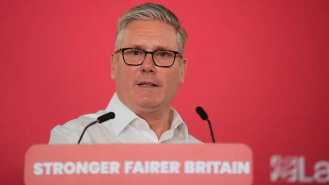 Starmer behind a lectern that has the words Stronger Fairer Britain on it