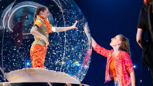A dancer reaches out to a small child inside a snow globe, during a performance by Austrian dance troupe Zucaroh