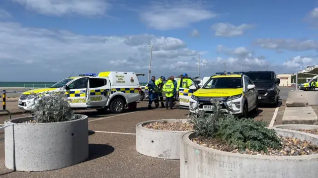 A landscape image showing coastguard and police vehicles by the seafront