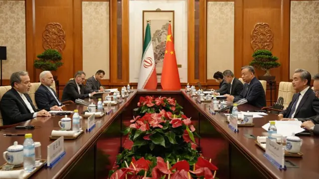 Chinese and Iranian officials sit across each other at a long table