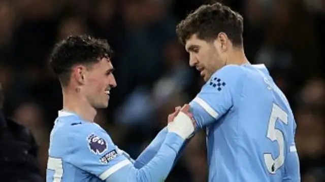 hil Foden puts the captain's armband onto the arm of Manchester City's English defender #05 John Stones