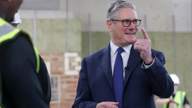 A smiling Starmer raises a finger as he gestures with his left hand