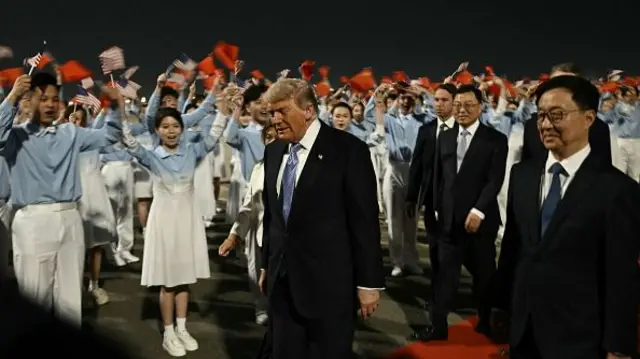 Donald Trump is escorted by China's Vice-President Han Zheng upon his arrival at Beijing Capital Airport in Beijing on May 13, 2026. Flag wavers hold Chinese and US flags in the background.