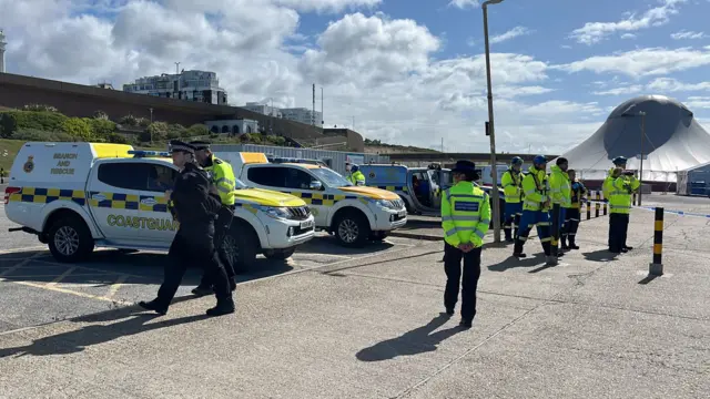 A number of officers stand in the carpark near to coastguard vehicles