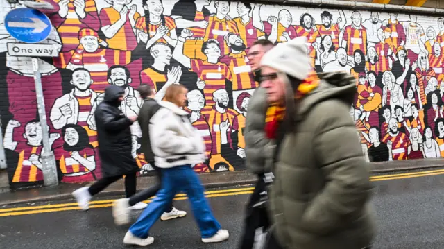 Fans outside Valley Parade walk past a Bradford City mural