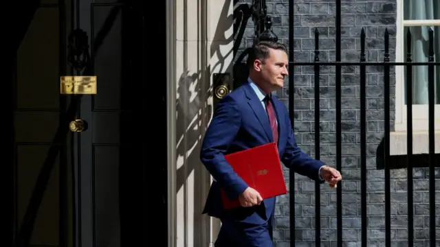 Wes Streeting leaves 10 Downing Street wearing a blue suit with a red tie. He is holding a red folder