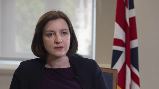 Phillipson speaks to a reporter whilst at in front of a Union Jack
