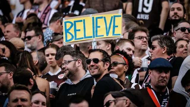 Fans of FC St. Pauli hold a sign reading 'Believe'