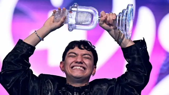 JJ, Austria's winning contestant last year, in a black outfit holding his trophy over his head