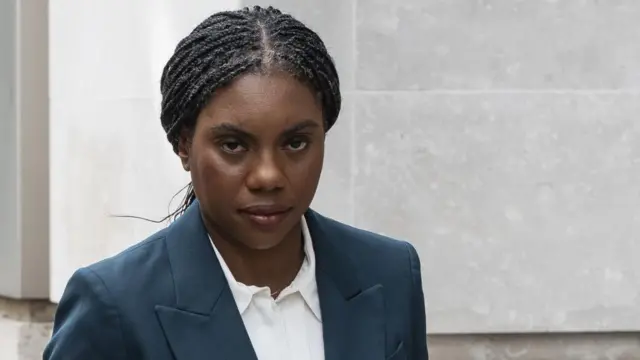 Badenoch pictured walking outside. She's looking towards the camera, wearing a dark blue suit and white shirt while walking outside