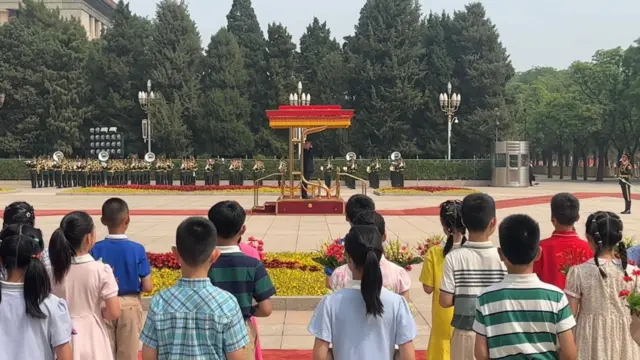 Rows of children watch as Trump salutes military officers.