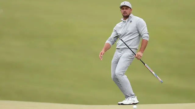 Bryson DeChambeau bends his knees as a putt just misses the hole