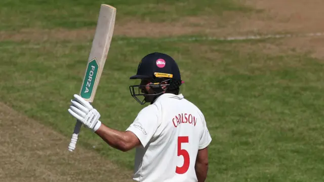 Glamorgan batter Kiran Carlson raises his bat to acknowledge applause after scoring a half-century