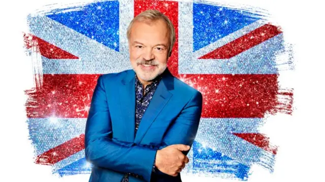 Graham Norton in a blue suit with the Union flag behind him