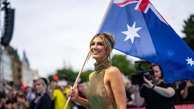 Delta Goodrem in a gold halterneck chainmail dress holding the Australian flag