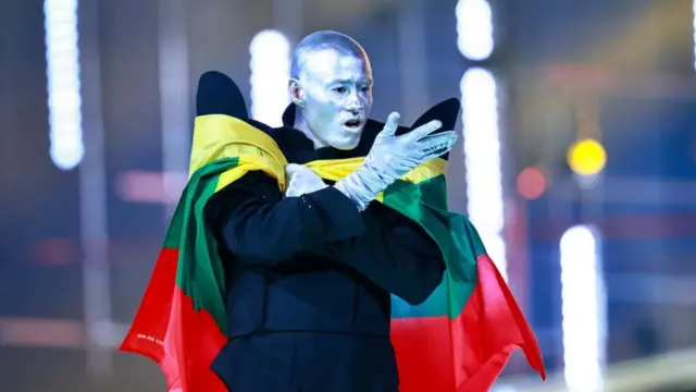 Lion Ceccah has a silver painted face and silver gloves, with a Lithuanian flag draped around his shoulder