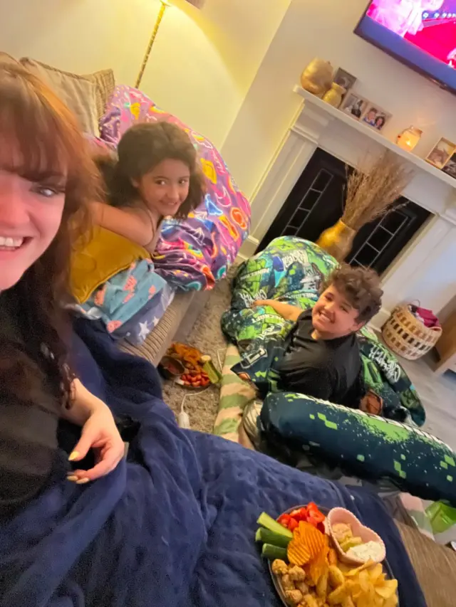Children and a woman in their living room with snacks and smiles