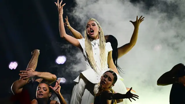 Monroe in a white dress reaching up and belting a song with dancers around her